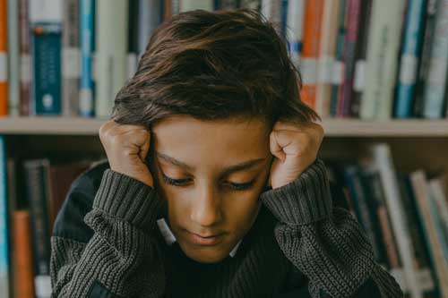 A kid looking down with his hands to the side of his head